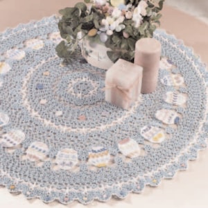 Könnte beinhalten: Eine zarte blaue Häkeldeckchen mit einem gewellten Rand und einem floralen Muster. Die Deckchen ist mit kleinen blauen und weißen Blumen verziert und perfekt, um jedem Tisch einen Hauch von Eleganz zu verleihen.