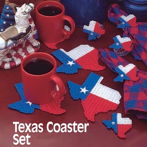May include: Set of six Texas-shaped coasters featuring the Texas flag in red, white, and blue. The coasters are made of plastic canvas and are perfect for protecting your furniture from hot or cold drinks. The coasters are displayed on a red surface with two mugs and a small American flag.