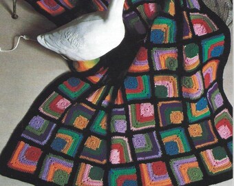 May include: A vibrant, crocheted blanket with a black border. The blanket showcases a patchwork design of squares in various colours, including red, orange, green, and purple. A white goose figurine rests on the blanket.