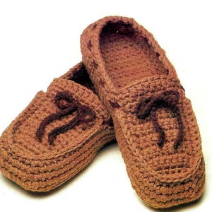 May include: A pair of brown crocheted slippers with a loafer style. The slippers have brown laces and a brown crocheted design.