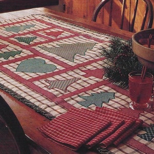 Peut inclure: Une décoration de table de Noël avec un chemin de table à carreaux orné d'arbres de Noël et de cœurs appliqués. Des serviettes rouges et des tasses d'une boisson rouge avec des bâtons de cannelle créent une ambiance festive.