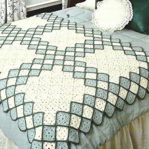 May include: A handmade crochet blanket in a diamond pattern. The blanket features a cream-colored center with light blue and dark green diamond-shaped borders. The blanket is displayed on a bed with a light blue bedspread.