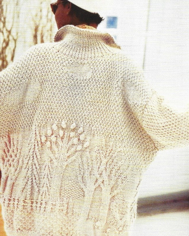 May include: A cream knitted cardigan with a textured design featuring trees and branches. The cardigan has a high neck and long sleeves.