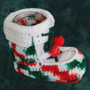 May include: White crocheted Christmas stocking with red and green stripes and a red pom-pom. The stocking is designed to hold a small jar or candle.