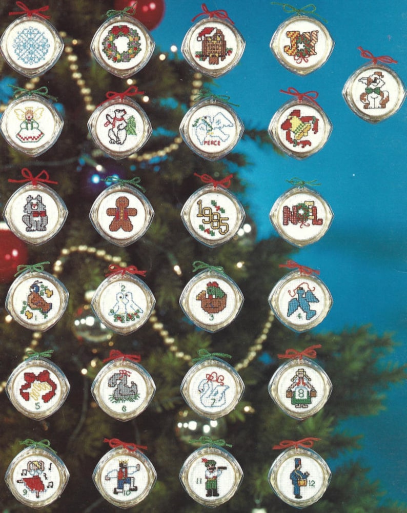 Peut inclure: Un ensemble de 12 d&eacute;corations de No&euml;l sur le th&egrave;me des f&ecirc;tes, comprenant un bonhomme en pain d'&eacute;pices, une colombe, un bonhomme de neige et un renne. Chaque d&eacute;coration est un cercle blanc avec un ruban rouge et un num&eacute;ro de 1 &agrave; 12.