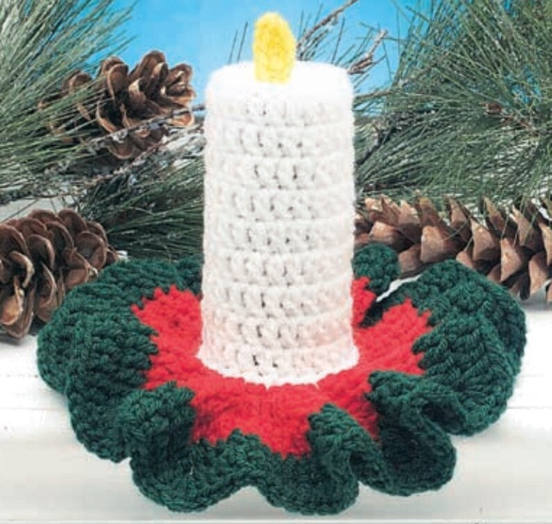 May include: A crocheted candle holder with a white candle and a green and red base. The base is made of crocheted fabric and has a ruffled edge.