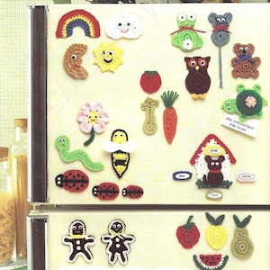 Puede incluir: Una colección de imanes de crochet con varios diseños, incluyendo un arcoíris, una nube, un sol, una luna, una flor, una abeja, una mariquita, un gusano, una zanahoria, un tomate, una rana, una tortuga, un búho, un oso, un hombre de jengibre, una fresa, un limón, una pera y una sandía. Los imanes se muestran en una puerta de refrigerador blanca.