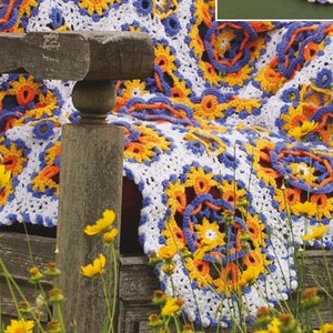 May include: A crocheted throw blanket with a white background and colorful floral designs in shades of orange, yellow, and blue. The blanket is draped over a wooden bench and surrounded by yellow flowers.
