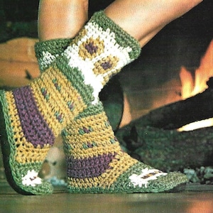 May include: Crocheted slipper boots in shades of green, yellow, purple, and white. The boots feature a floral design on the upper portion and a solid sole. The boots are shown near a fireplace.
