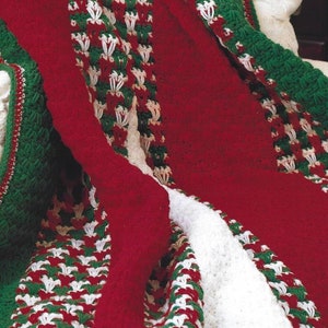 May include: A red, white, and green crocheted throw blanket with a textured pattern. The blanket is folded and draped over a white armchair.