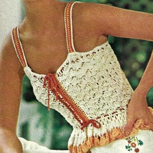 Peut inclure: Un haut crocheté de couleur blanche et orange. Le haut présente un motif en dentelle et un ourlet à volants. Les bretelles sont en fil blanc et orange.