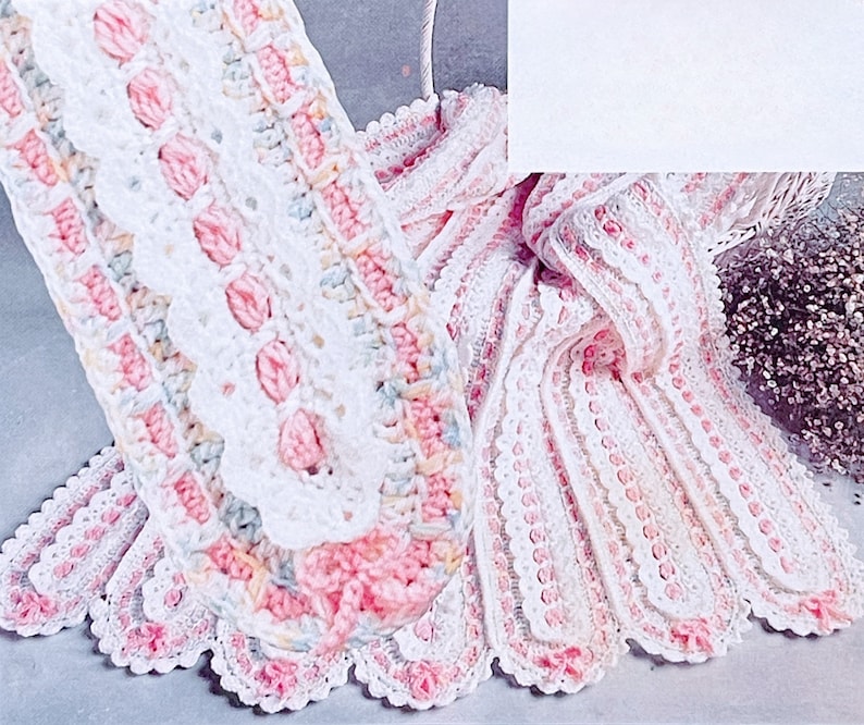 Puede incluir: Una manta de beb&eacute; de ganchillo blanca con detalles en rosa y amarillo. La manta tiene un borde festoneado y un delicado patr&oacute;n de encaje.