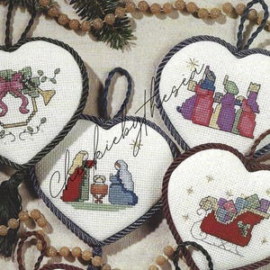 May include: Four heart-shaped Christmas ornaments with cross-stitch designs. The ornaments feature a nativity scene, a sleigh with presents, a star, and a bell with a bow.