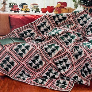 May include: A handmade, crocheted blanket with a repeating pattern of green Christmas trees within diamond shapes. The blanket features red, white, and black accents, draped over a brown couch. Two green books rest on the blanket.
