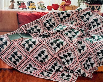 May include: A handmade, crocheted blanket with a repeating pattern of green Christmas trees within diamond shapes. The blanket features red, white, and black accents, draped over a brown couch. Two green books rest on the blanket.
