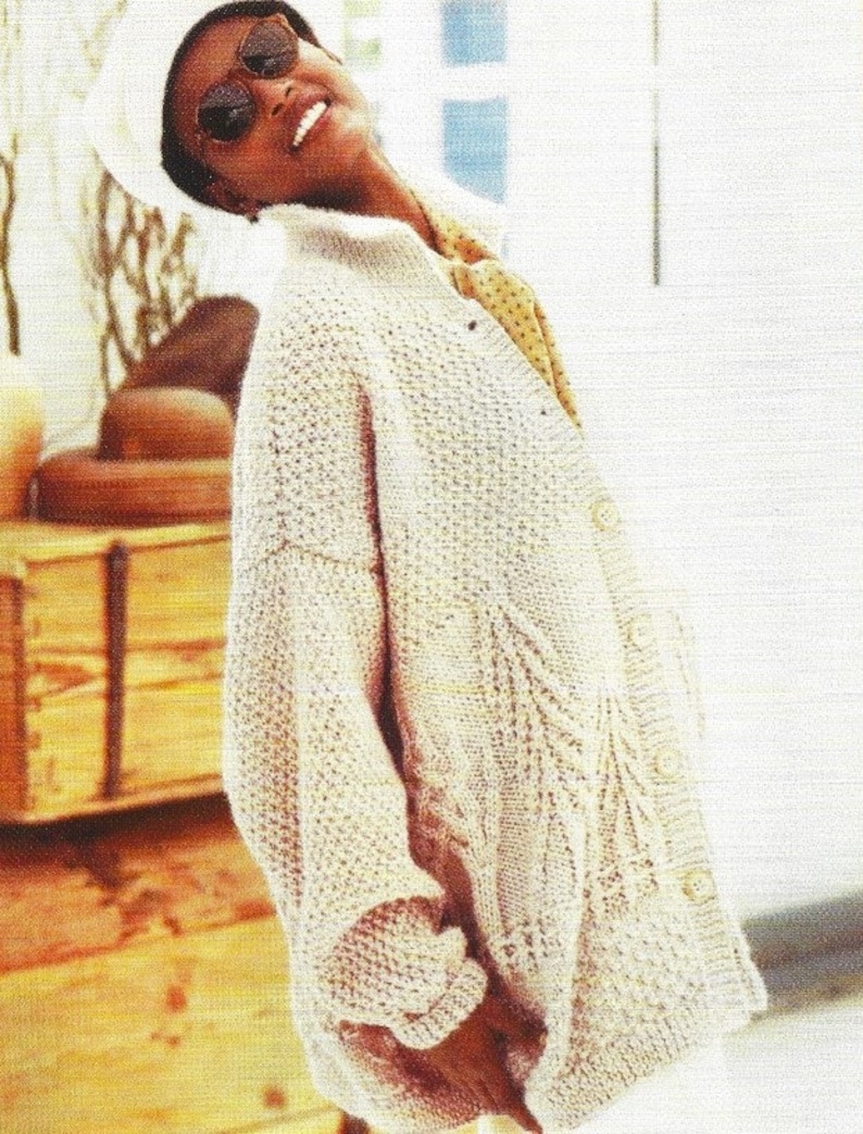 May include: A light beige knitted cardigan with a cable knit pattern and button closure. The cardigan is oversized and has a relaxed fit.