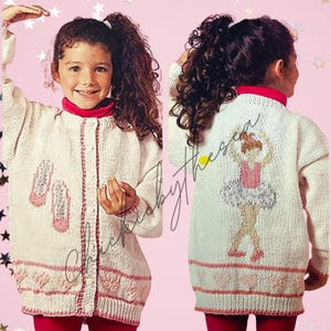 May include: A white knitted cardigan with a pink trim and a ballerina design on the back. The cardigan has a button closure and is shown being worn by a child.