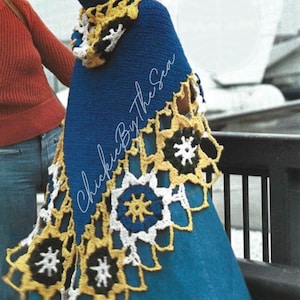 Puede incluir: Una capa azul con capucha y un ribete decorativo de ganchillo en amarillo, blanco y negro. La capa tiene el texto "Chickie By The Sea" en cursiva. La capa se lleva sobre un vestido vaquero.