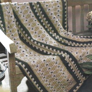 May include: A rectangular crochet blanket featuring alternating vertical stripes of dark forest green, cream, and muted gold yarn. The design incorporates textured stitch patterns and decorative floral-like motifs arranged in repeating rows.