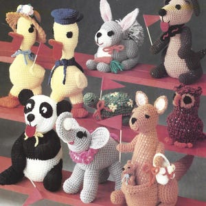 Peut inclure: Collection de jouets animaux crochetés à la main, dont un canard, un lapin, un chien, un panda, un éléphant, un kangourou avec son petit et un hibou. Les jouets sont de couleurs variées, comme le jaune, le gris, le marron et le noir, et sont disposés sur une étagère rouge.