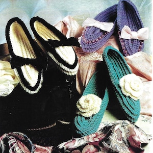 Puede incluir: Una colección de zapatillas de ganchillo hechas a mano en varios colores. Las zapatillas incluyen mocasines blancos y negros con lazos, zapatillas moradas con lazos rosas y zapatillas verde azulado con detalles de flores color crema. Las zapatillas se exhiben sobre una tela estampada.