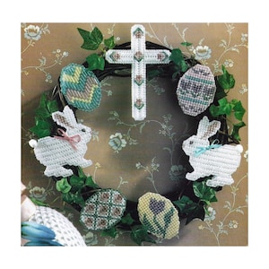 May include: A white plastic Easter wreath with a cross, two white bunnies, and four decorated eggs. The wreath is made of grapevine and is decorated with green ivy.