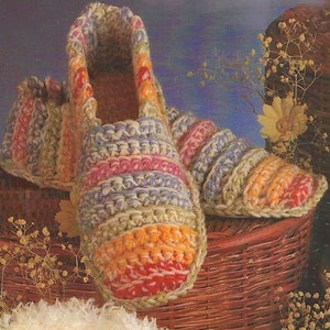 May include: A pair of crocheted slippers with a striped pattern in shades of green, purple, orange, and red. The slippers are sitting on a wicker basket.