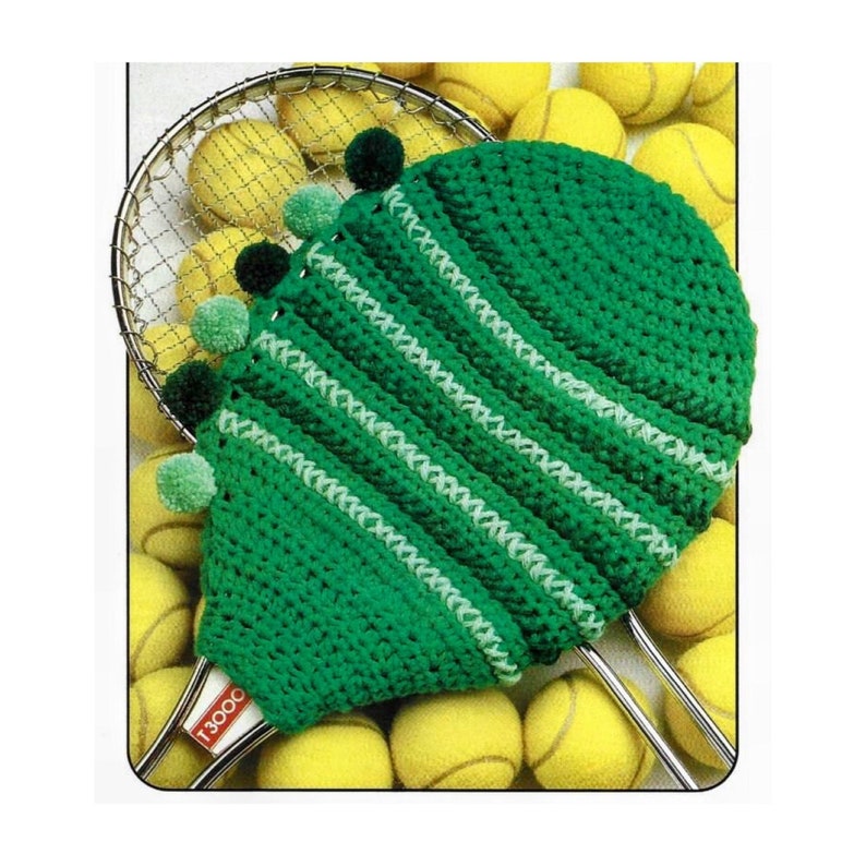 May include: A green crocheted tennis racket cover with white stripes and pom-poms. The cover is on top of a tennis racket and surrounded by yellow tennis balls.
