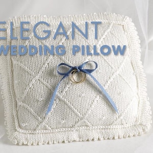 May include: White knitted wedding ring pillow with a blue satin ribbon and two gold rings. The pillow has a diamond pattern and a crocheted border. The text "ELEGANT WEDDING PILLOW" is displayed above the pillow.