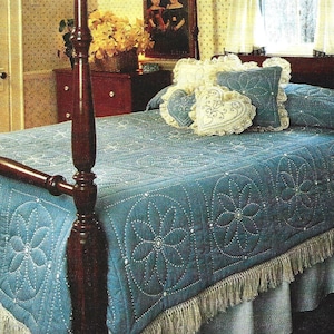 May include: A blue quilted bedspread with a white fringe trim and a white lace pillow with a heart design on a four-poster bed.