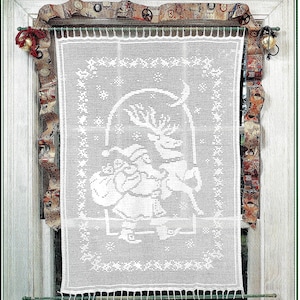 May include: A white crocheted Christmas curtain featuring Santa Claus riding a reindeer, with a decorative border and fringe. The curtain is hanging in a window decorated with festive ribbon and bells.