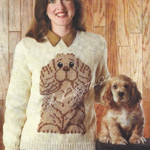 Puede incluir: Una mujer lleva un suéter de punto blanco con un diseño de perro marrón. El suéter tiene un cuello marrón y el perro lleva un collar marrón. La mujer está de pie junto a un cocker spaniel marrón y blanco.