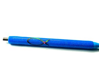 May include: A blue glitter pen with a decorative design. The pen features a blue barrel with a silver tip and a blue conical tip. The design on the pen includes a black and green ribbon with a pink gem.