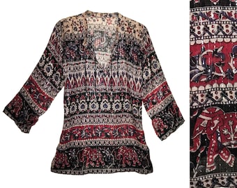 May include: A long-sleeved tunic top with a V-neck and a colorful, patterned design. The fabric features a mix of red, black, and cream colors with floral and elephant motifs. The sleeves are flared.