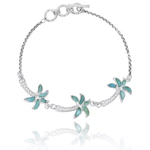 May include: A silver bracelet with a delicate chain and three palm tree charms. The palm trees are made of turquoise and white stones.