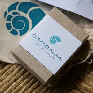 May include: A small, brown cardboard box with a white label. The label has the text "Oceano Azure Sea Life Jewelry" and a blue and green seashell logo.