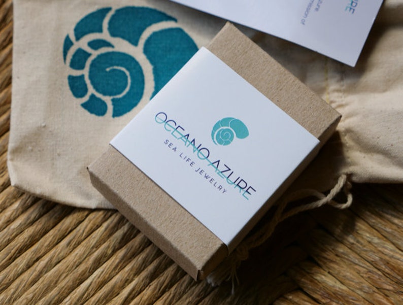 May include: A small, brown cardboard box with a white label. The label has the text "Oceano Azure Sea Life Jewelry" and a blue and green seashell logo.