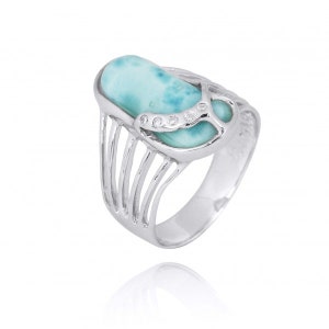 May include: A silver ring with a light blue oval gemstone set in a decorative silver setting. The ring has a delicate, intricate design with a series of vertical lines on the band.