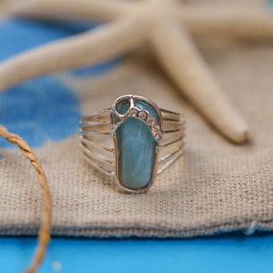May include: A silver ring with a blue gemstone in the shape of a flip-flop. The gemstone is accented with small clear rhinestones.