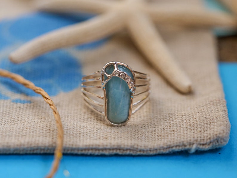 May include: A silver ring with a blue gemstone in the shape of a flip-flop. The gemstone is accented with small clear rhinestones.