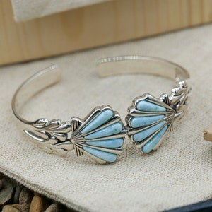 May include: A silver bracelet featuring two turquoise shell designs. The bracelet is open and has a delicate floral design on the side.