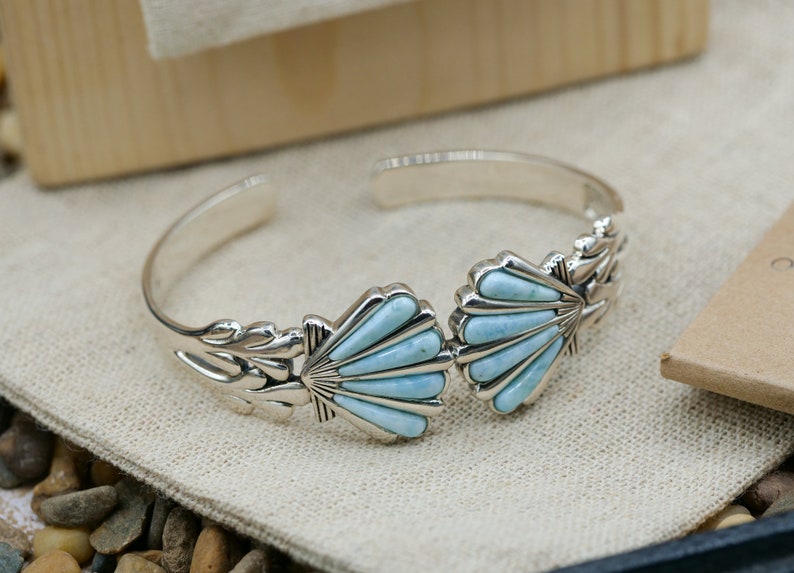 May include: A silver bracelet with two turquoise shell designs. The bracelet is open and has a delicate floral design on the side.