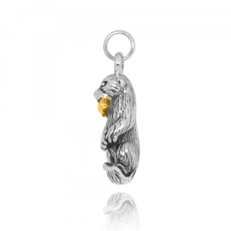 May include: Silver charm of an otter holding a fish in its mouth. The fish is made of gold. The charm has a loop at the top for attaching to a necklace or bracelet.