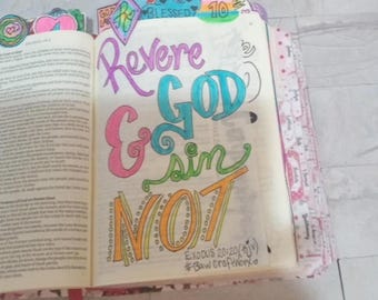Könnte beinhalten: Nahaufnahme einer Seite in einer Bibel mit farbigem handgeschriebenem Text, der "Verehre Gott und sündige nicht" lautet. Der Text ist von bunten Herzen und anderen Verzierungen umgeben. Der Bibelvers "Exodus 20:20 (KJV)" und der Hashtag "#Baw craftworx" stehen unter dem Text.