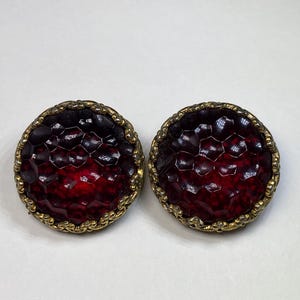 May include: A pair of red glass earrings with a gold-toned metal setting. The glass is textured and has a honeycomb pattern.