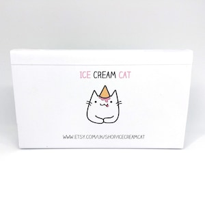 Puede incluir: Caja blanca con un gato de dibujos animados que lleva un cono de helado en la cabeza. El texto "ICE CREAM CAT" est&aacute; por encima del gato y "www.etsy.com/uk/shop/icecreamcat" est&aacute; por debajo del gato.
