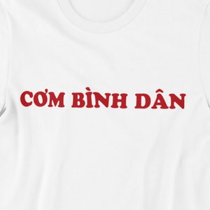 May include: White t-shirt with the text "CƠM BÌNH DÂN" printed in red.