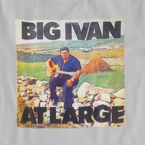May include: A white t-shirt with a colorful image of a man playing a guitar. The image has the text "BIG IVAN AT LARGE" printed on it.