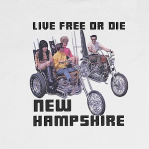 Puede incluir: Una camiseta blanca con un gráfico negro de un grupo de personas montando una motocicleta. El texto "Live Free or Die" y "New Hampshire" está impreso en la camiseta.