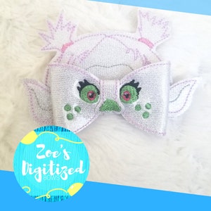 May include: A glittery, light purple hair bow in the shape of a cartoon character with green eyes and a bow-tie design. The bow has a round, blue logo that says "Zoe's Digitized Bows".